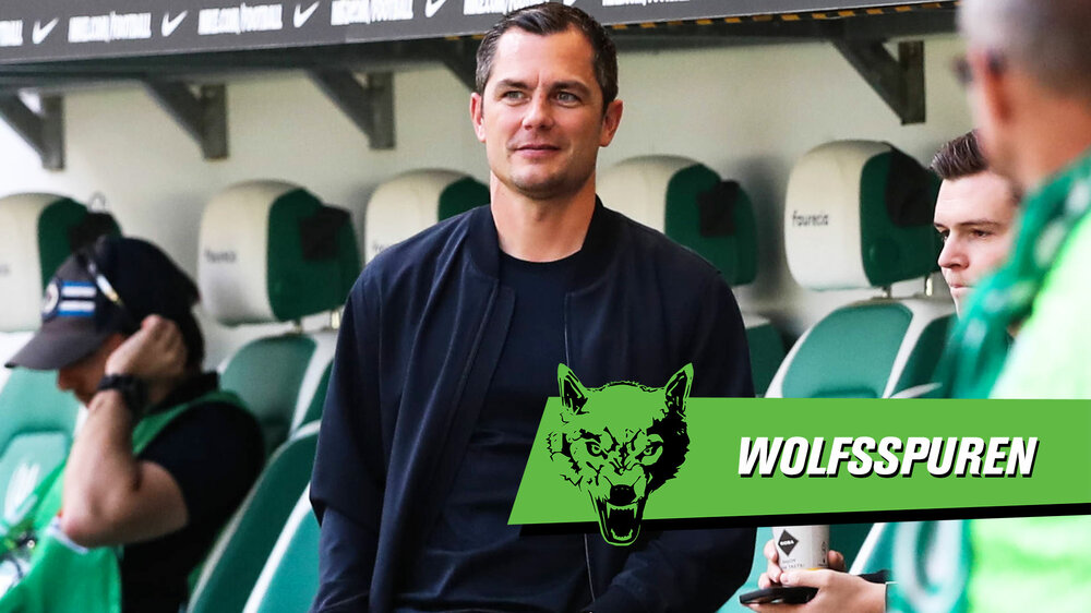 Der VfL-Wolfsburg-Geschäftsführer Marcel Schäfer steht glücklich an der Seitenlinie der Volkswagen-Arena. Auf der rechten Bildhälfte ist das Logo der Wolfsspuren zu sehen.