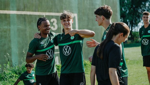 Spieler der U19 vom VfL Wolfsburg liegen sich lachend in den Armen und lächeln in die Kamera.