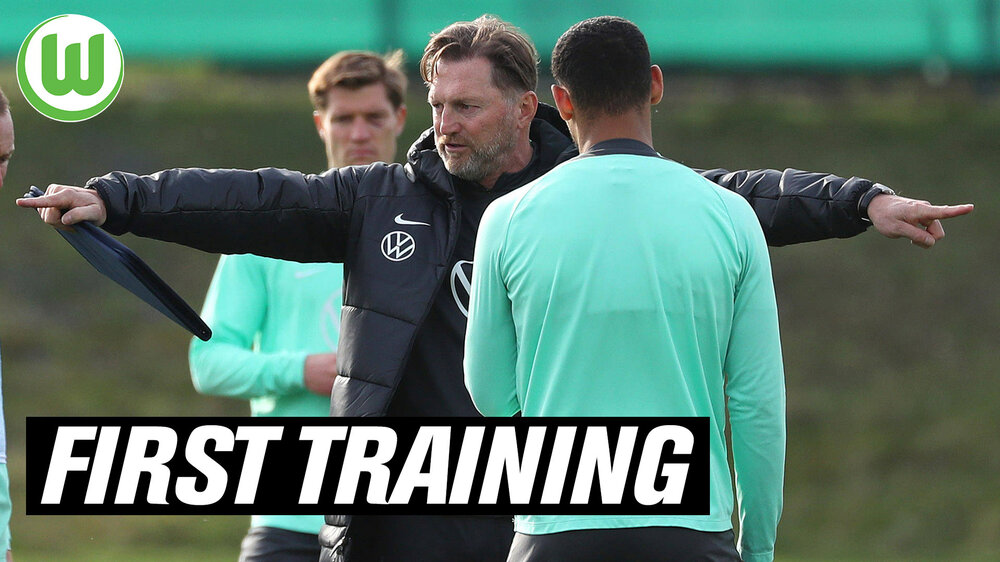 Der Trainer Ralph Hasenhüttl vom VfL Wolfsburg streckt seine beiden Arme aus und zeigt nach außen. Davor befindet sich der Schriftzug "First Training".