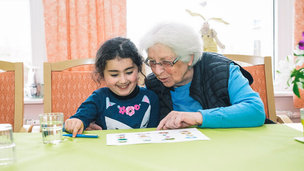 Die Dame aus dem AWO Wohnheim berät im Rahmen des VfL-Wolfsburg-Besuchs das kleine Mädchen beim Bingo spielen.