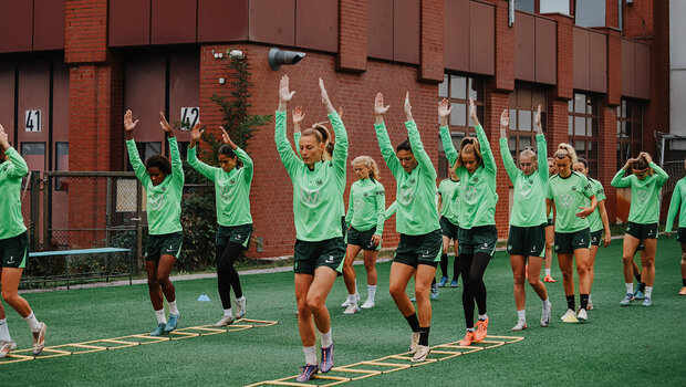 Auf dem Trainingsplatz liegen zwei Sprossenleitern. Die VfL-Wolfsburg-Spielerinnen laufen hintereinander, mit nach oben gestreckten Armen, durch die Sprossenleiter. 