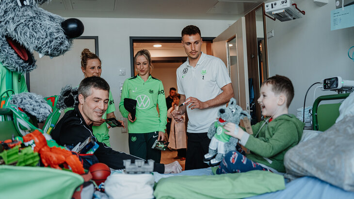 VfL-Wolfsburg Spielerinnen Kathy, Svenni und Spieler Kili und Wölfi besuchen einen kleinen Jungen auf der Kinderstation.