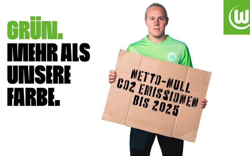 VfL Wolfsburg Spieler Xaver Schlager trägt ein Race to Zero Plakat in den Händen.