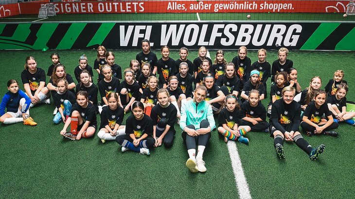 Jule Brand sitzt mit einigen Mädchen auf dem Boden im Bolzwerk des VfL Wolfsburg.