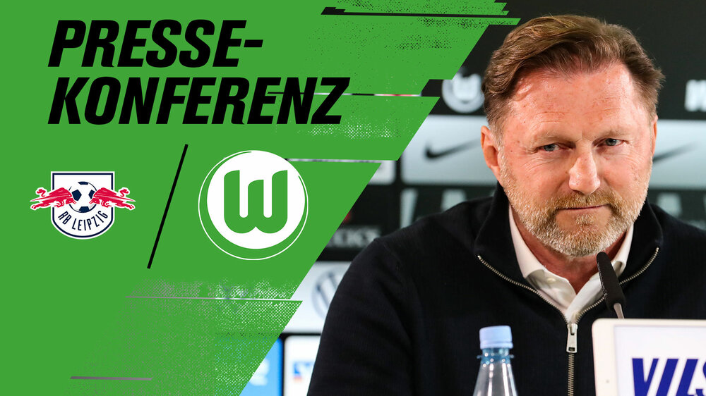 VfL Wolfsburg Trainer Ralph Hasenhüttl sitzt bei einer Pressekonferenz am Pult und schaut ernst in die Kamera.