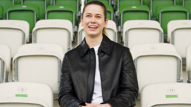 VfL Wolfsburg Neuzugang Stina Johannes sitzt auf der Tribüne im AOK Stadion und lächelt in die Kamera.