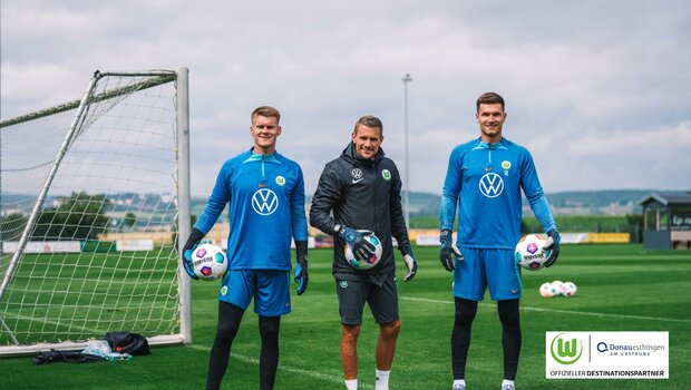 Zwei Torhüter und ihr Trainer des VfL Wolfsburg posieren vor dem Tor.