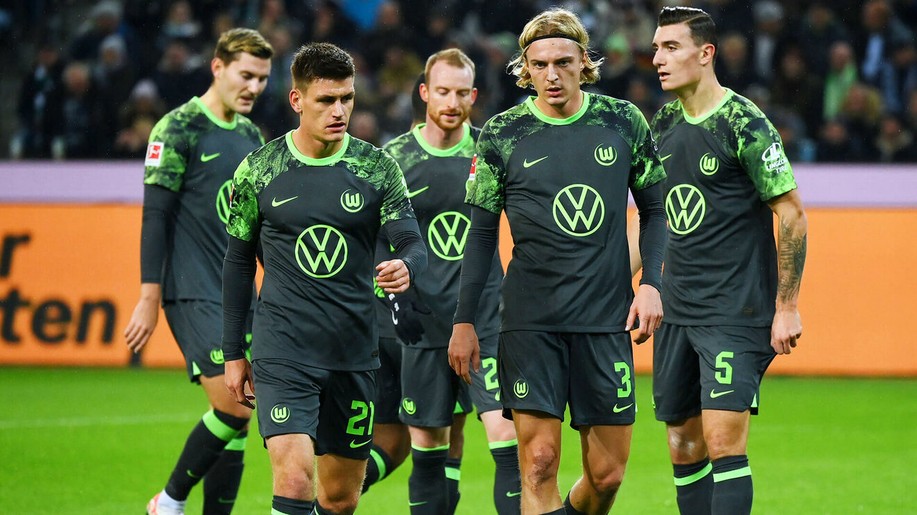 Spieler des VfL Wolfsburg gehen gemeinsam über den Rasen.