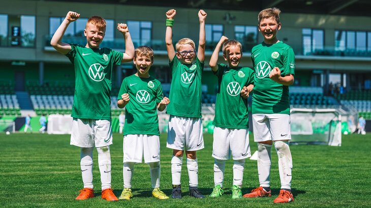 Fünf Jungs in VfL-Wolfsburg-Leibchen stehen auf dem Rasen, ballen ihre Fäuste und jubeln.
