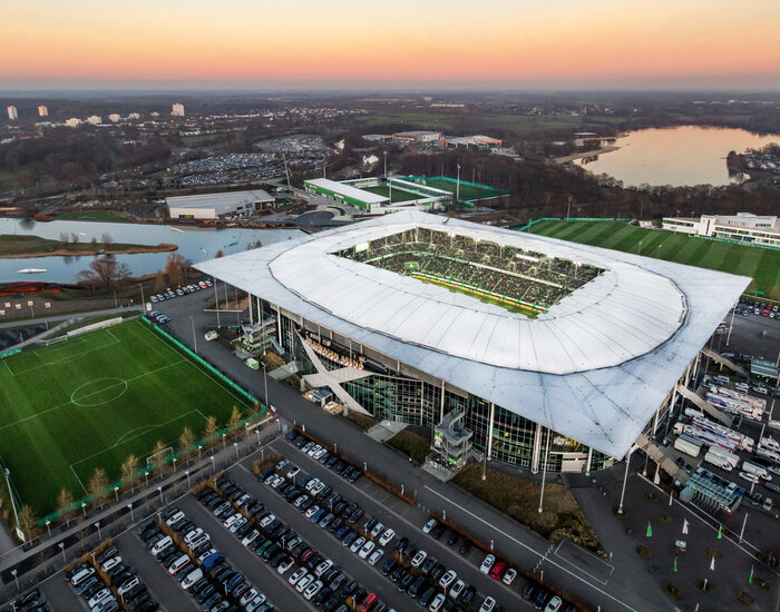 Das Stadion des VfL Wolfsburg sowie die Trainingsplätze, der Allerpark und der Allersee von oben bei Sonnenuntergang.