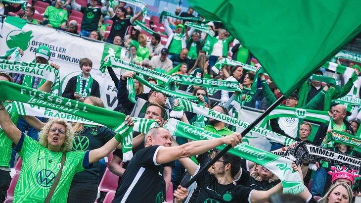 Die Fans der Frauenmannschaft des VfL Wolfsburg halten grün-weiße Schals und Fahnen in die Höhe.
