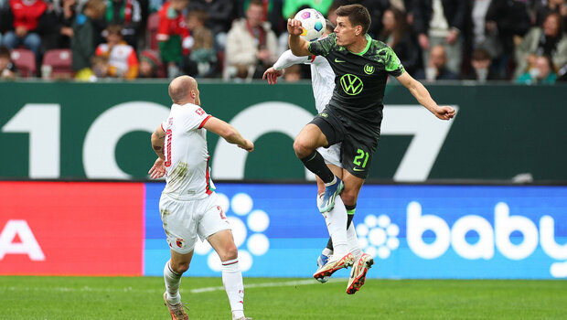 VfL-Wolfsburg-Spieler Maehle springt hoch in einem Zweikampf mit einem Augsburg-Spieler.