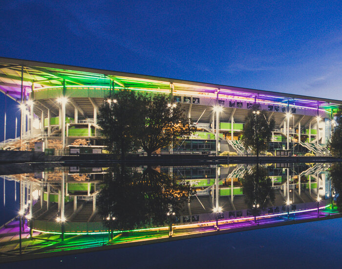 Ein Volkswagen Arena des VfL Wolfsburg aus Sicht der Arena Sees erleuchtet in Regenbogenfarben.
