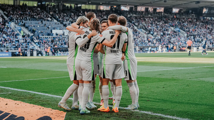 Spieler des VfL Wolfsburg stehen gemeinsam im Stadion und haben sich gegenseitig in den Armen.