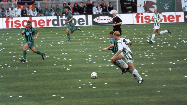 Spielsituation. Ein VfL-Spieler und ein Gladbach-Spieler sind auf Augenhöhe am Ball. Drei Spieler sind um die beiden herum positioniert und bereit den Ball anzunehmen. Auf dem Platz liegt weißes Konfetti.
