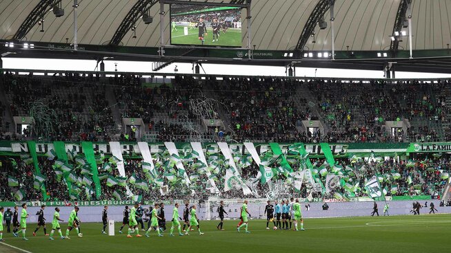 Die Wölfe laufen mit ihren Gegnern, dem DSC Arminia Bielefeld in die Volkswagen Arena ein. Die Ränge sind voll von Fans und Fahren.