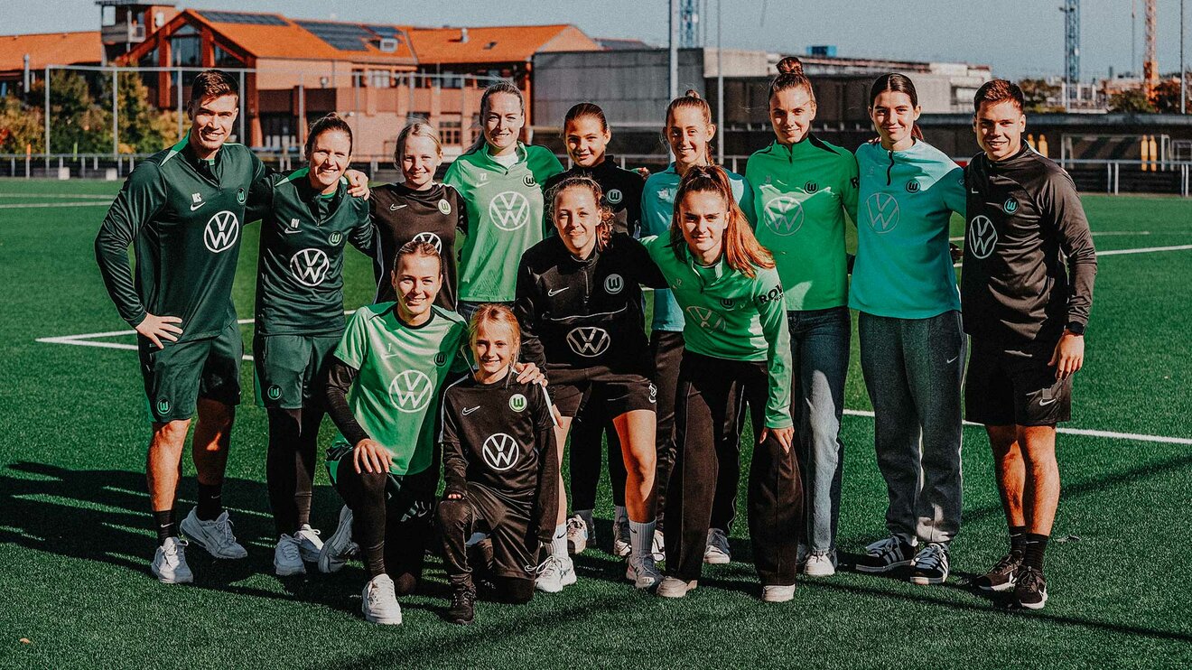 VfL-Wolfsburg-Torhüterinnen verschiedener Mannschaften sowie ihre Trainer*innen stehen gemeinsam auf dem Trainingsplatz.