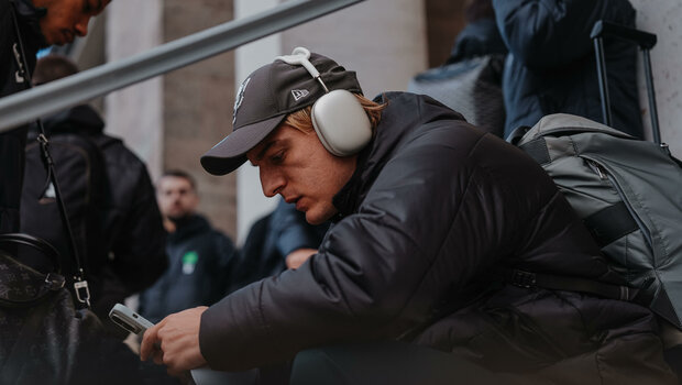 Der VfL-Wolfsburg-Spieler Sebastiaan Bornauw sitzt auf einer Treppenstufe und hält sein Handy in der Hand.