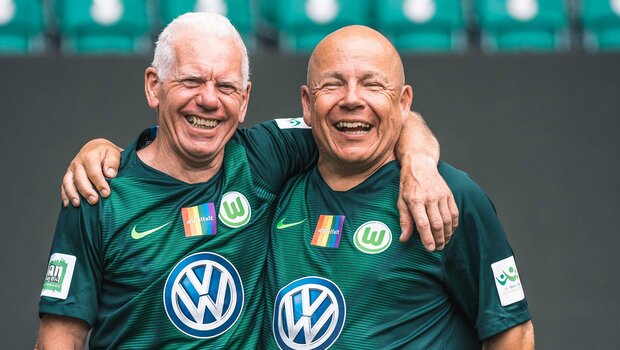 Zwei Spieler des VfL-Wolfsburg-Walking-Footballs lächeln und haben die Arme umeinander gelegt.