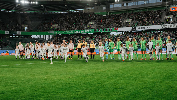 Die Teams der VfL-Wolfsburg-Frauen sowie des FC Bayern München stehen in einer Reihe in der Mitte der Volkswagen Arena. Die Einlaufkinder laufen weg von ihnen.