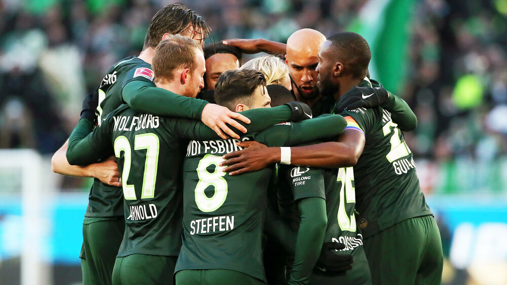 Jubelnde Spieler des VfL Wolfsburg umarmen sich nach einem Tor während eines Heimspiels. 