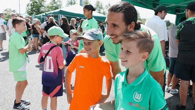 Ein Spieler des VfL Wolfsburg posiert beim VfL Familienfest mit zwei kleinen Fans für ein Foto.