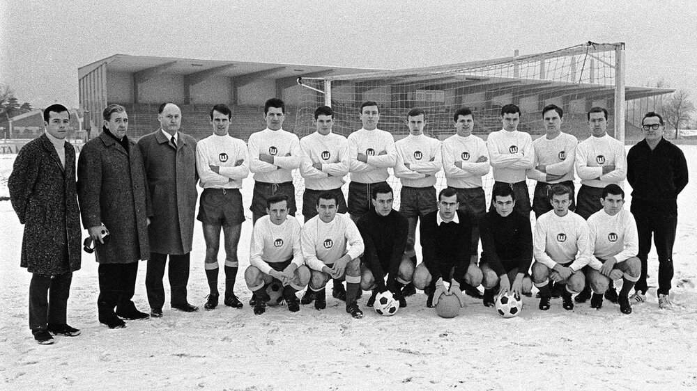 Die ehemalige VfL Wolfsburg Herrenmannschaft von 1967 positioniert sich im Winter für ein Mannschaftsfoto auf dem beschneiten Feld.