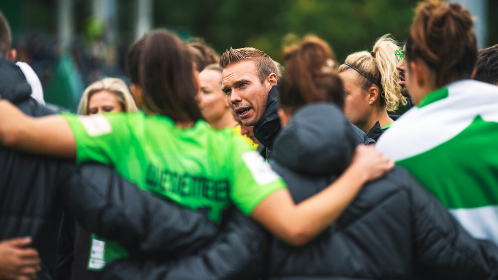 VfL-Wolfsburg-Trainer Tommy Stroot hält im Mannschaftskreis eine motivierende Ansprache bei einem Spiel.