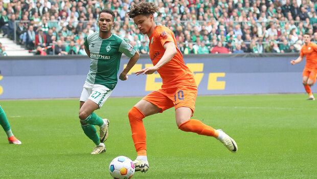 VfL Wolfsburg Spieler Kevin Paredes hat den Ball vor sich liegen und streckt sein linkes Bein nachhinten.