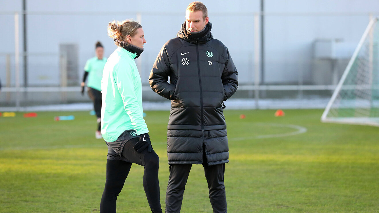 VfL Wolfsburg Trainer Stroot spricht auf dem Trainingsplatz mit einer Spielerin.