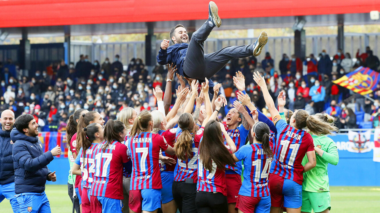 Die Spielerinnen des FC Barcelona Femeni jubeln auf dem Platz und tragen ihren Traininern auf Händen um ihn hoch leben zu lassen.