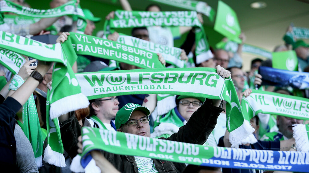 Die Fans der Frauenmannschaft des VfL Wolfsburg halten ihre Fanschals ausgestreckt in die Luft.