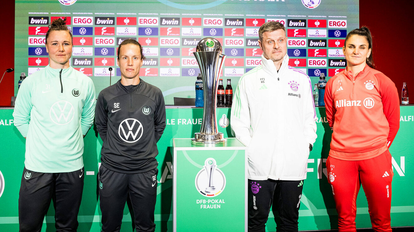 Die VfL-Wolfsburg-Spielerin Marina Hegering und Sabrina Eckhoff stehen neben dem DFB-Pokal und den Münchner Vertretern.