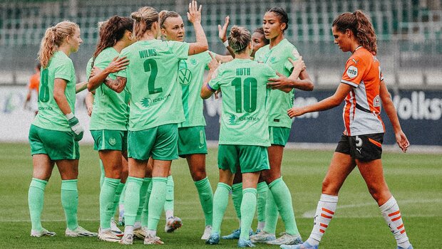 VfL-Wolfsburg-Spielerinnen stehen zusammen auf dem Rasen und liegen einander in den Armen.