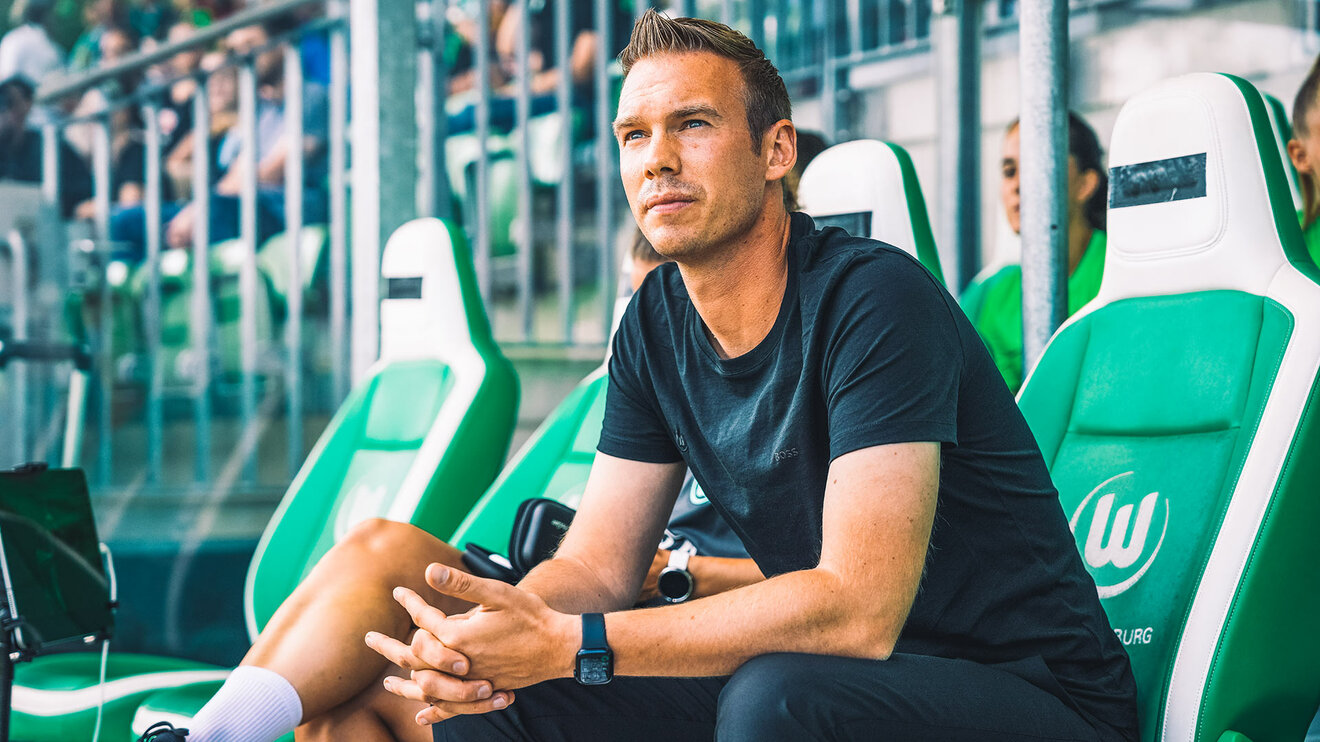 VfL-Wolfsburg-Cheftrainer der Frauen Tommy Stroot sitzt auf der Trainerbank und schaut nach vorne.