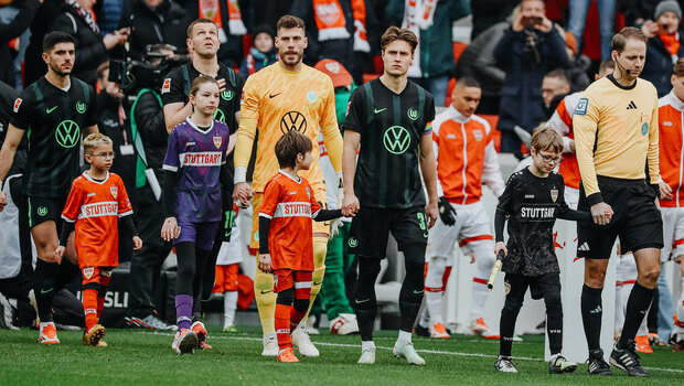 VfL-Wolfsburg-Spieler Mattias Svanberg geht mit einem Einlaufkind hinter dem Schiedsrichter aufs Feld.