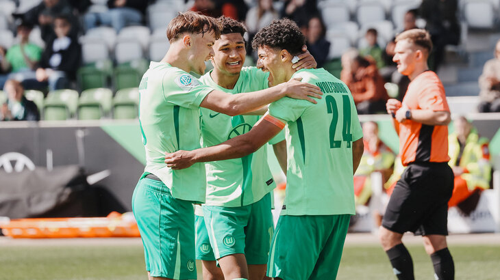 Drei Spieler der U19-Mannschaft des VfL Wolfsburg nehmen sich in den Arm und jubeln.