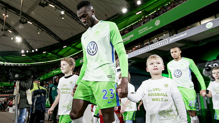 VfL Wolfsburg-Spieler Josuha Guilavogui läuft mit einem Kind an der Hand ins Stadion ein.