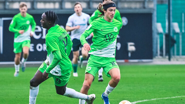 Zwei U19-Spieler des VfL Wolfsburg laufen über das Spielfeld, einer hat den Ball am Fuß.
