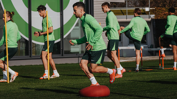Der VfL-Wolfsburg-Spieler Mohamed Amoura mit einem Bein auf einem roten Ball.