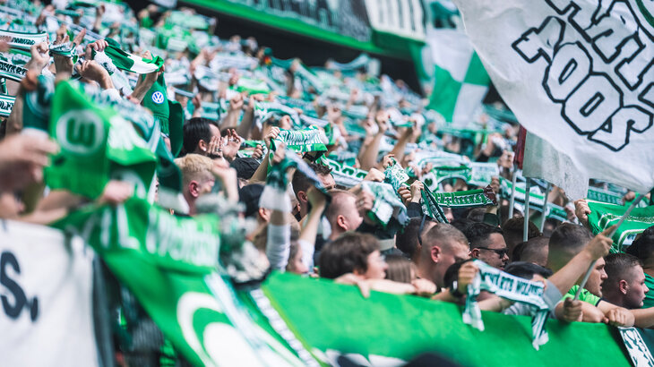 Viele Fans des VfL Wolfsburg, die ihre Schals in die Luft strecken.