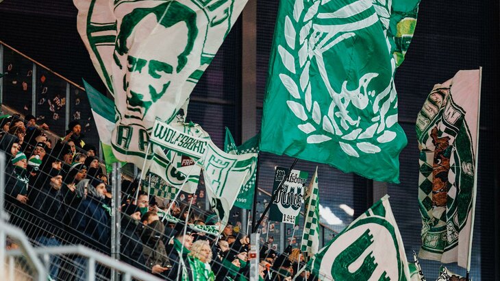 Fans des VfL Wolfsburg schwenken grün-weiße Fahnen.