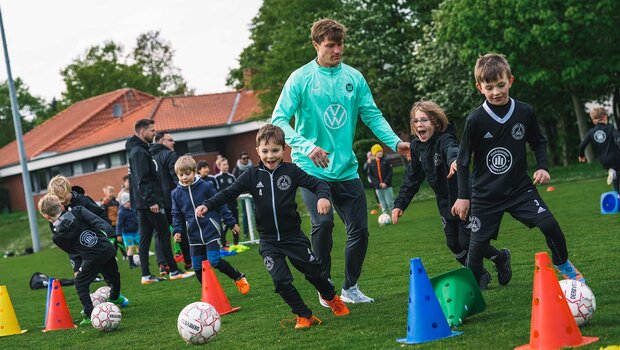 VfL-Wolfsburg-Spieler Kevin Behrens macht mit den Kindern eine Laufübung mit Ball.
