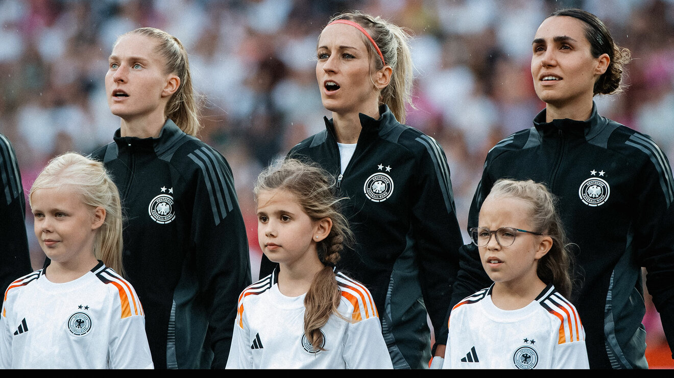 Kathy Hendrich steht mit Einlaufkindern auf dem Spielfeld vor einem Spiel der deutschen Nationalmannschaft.