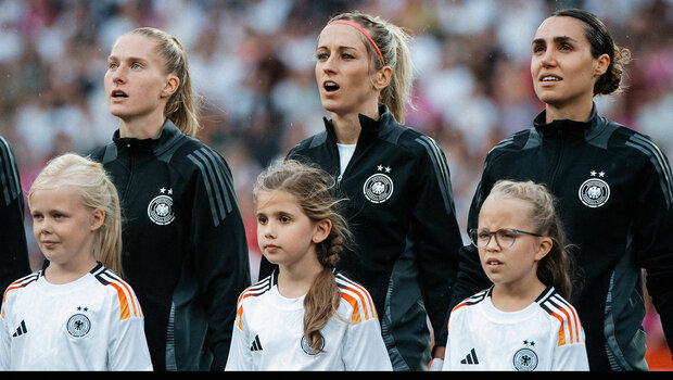 Kathy Hendrich steht mit Einlaufkindern auf dem Spielfeld vor einem Spiel der deutschen Nationalmannschaft.
