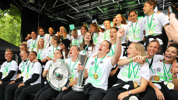 Die Doublesiegerinnen des VfL Wolfsburg feiern auf der Rathausbühne mit beiden Trophäen in den Händen.