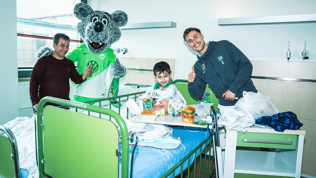 VfL-Wolfsburg-Spieler Kilian Fischer besucht gemeinsam mit Wölfi das Kinderkrankenhaus. Er macht ein Foto mit einem Patienten und seinem Vater.