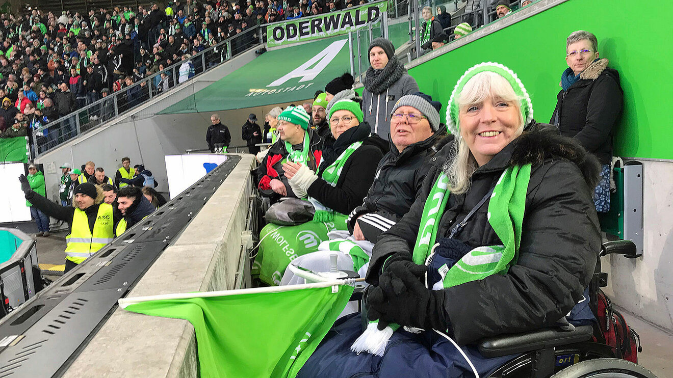 VfL Wolfsburg-Fans auf den Rollstuhlfahrerplätzen der Volkswagen Arena lachen in die Kamera.