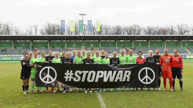 Die Mannschaft der Wölfinnen posiert vor Anpfiff der Partie des VfL Wolfsburg gegen SC Freiburg auf dem Spielfeld mit einem STOP WAR Banner.