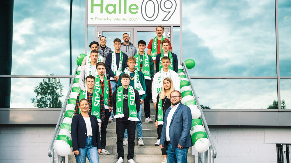 VfL Wolfsburg Campus angehörige posieren mit VfL Schals um den Hals auf der Treppe vor der Halle 09.